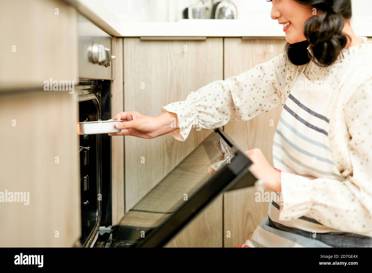 donna che indossa il forno mitt mettendo teglia con biscotti crudi in forno moderno in cucina domestica Foto Stock