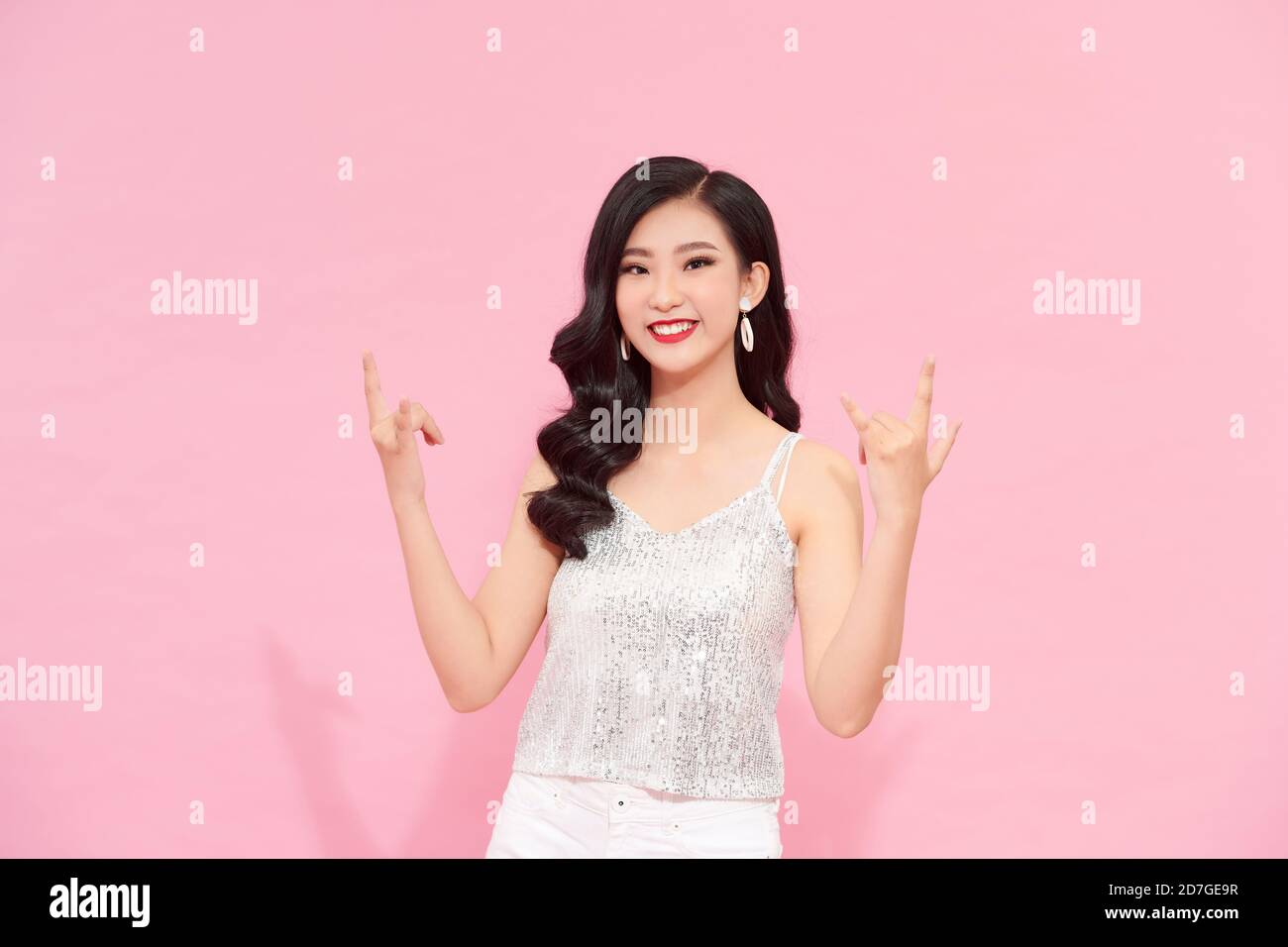 donna che posa in un lungo abito da festa in argento su sfondo rosa Foto Stock