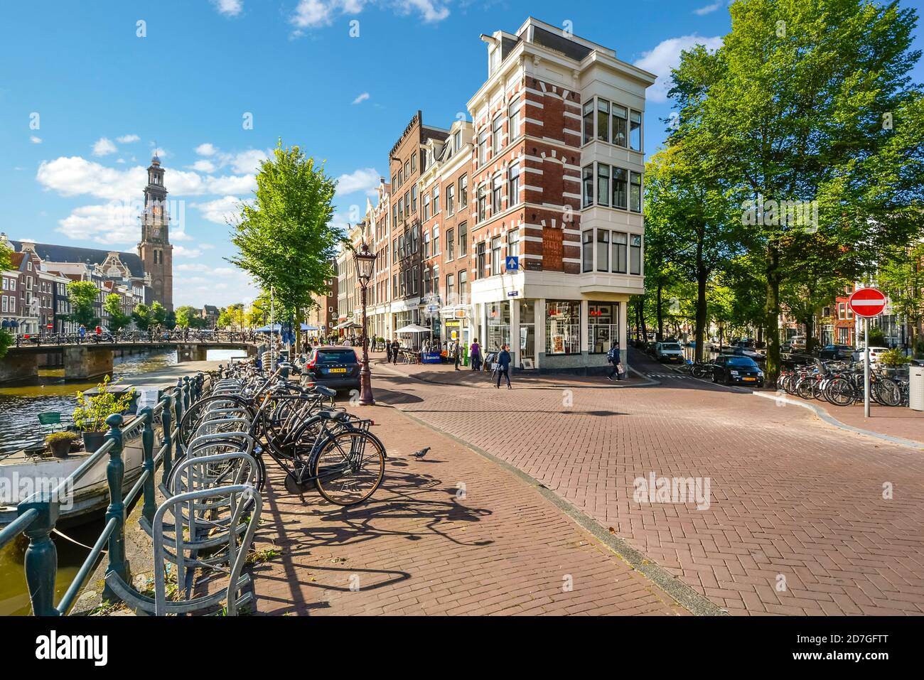 Biciclette parcheggiate lungo un canale vicino alla chiesa di Westerkerk AS i turisti potranno visitare i negozi e i ponti del centro storico Di Amsterdam Paesi Bassi Foto Stock