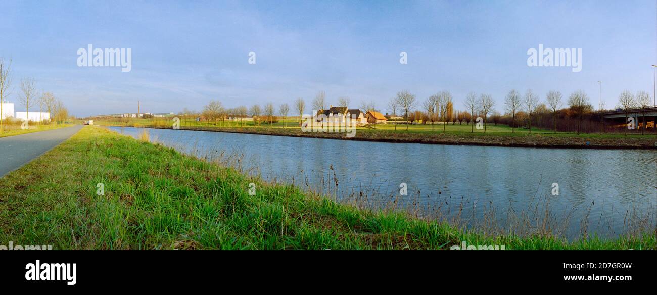 Vista panoramica su un fiume con alberi in inverno caldo luce prima del tramonto con un cielo azzurro couldless con un sacco di erba verde e fattoriali nella b Foto Stock