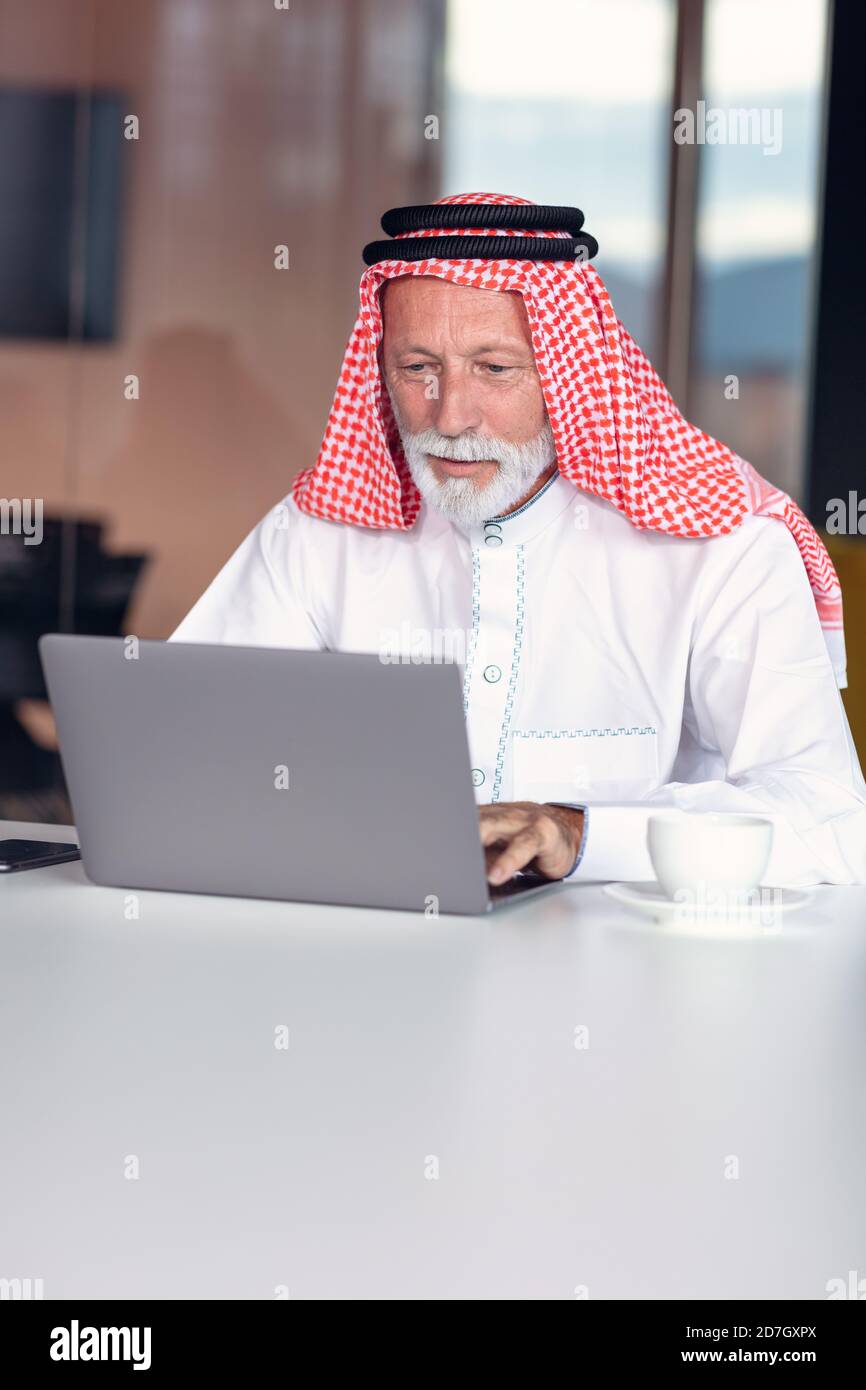Uomo d'affari arabo sicuro e sorridente in ufficio utilizzando un computer portatile. Foto Stock