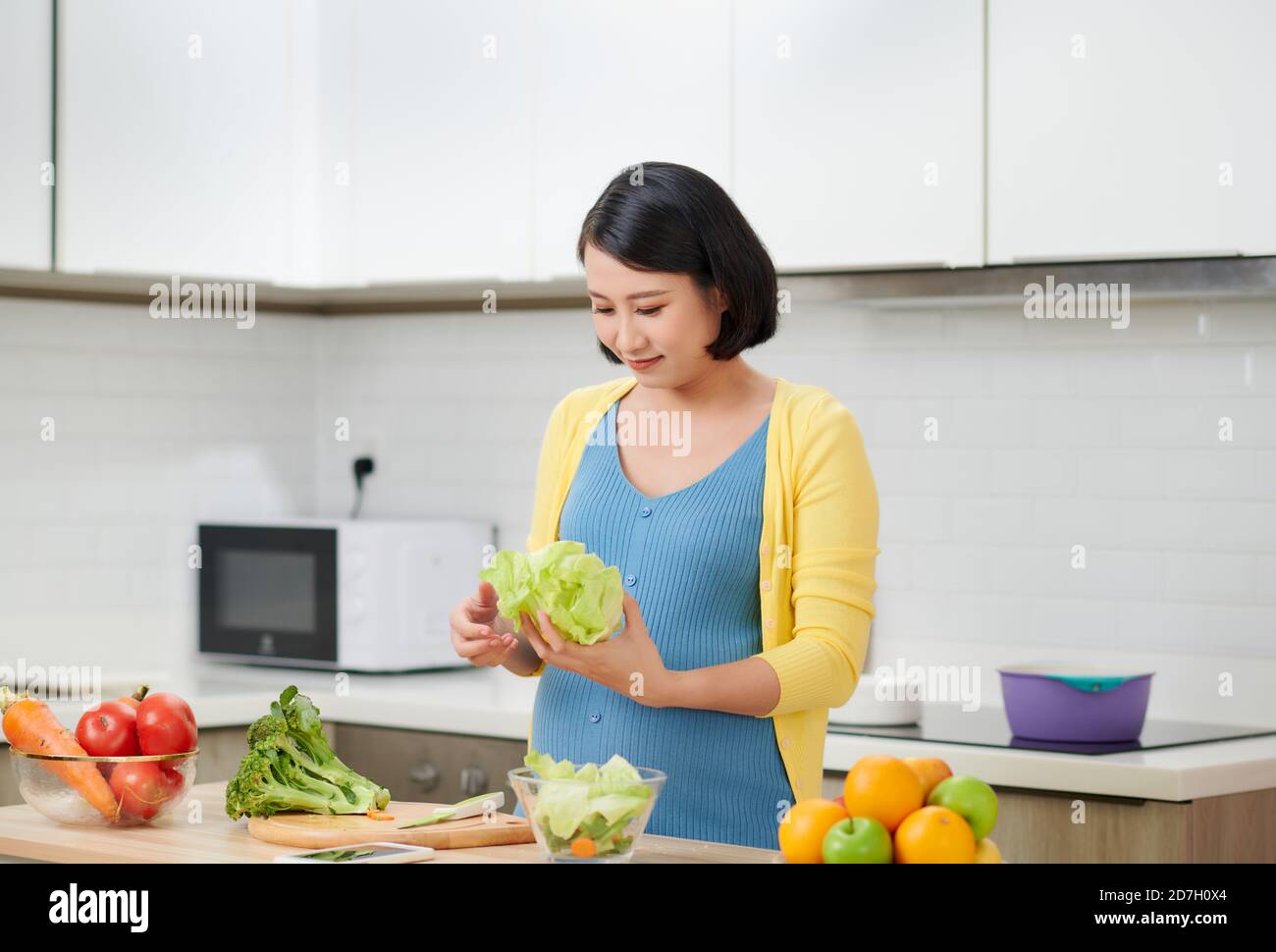 Felice donna incinta cottura a casa, facendo fresca insalata verde, mangiare molte verdure differenti durante la gravidanza, gravidanza sana nozione Foto Stock