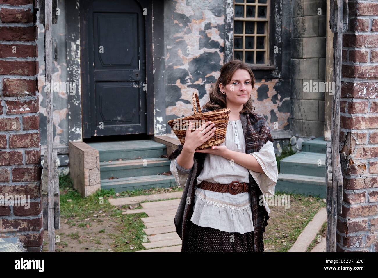 Donna in abiti antichi tiene un cesto al legno wicket di una casa nello stile di 18-19 secoli Foto Stock