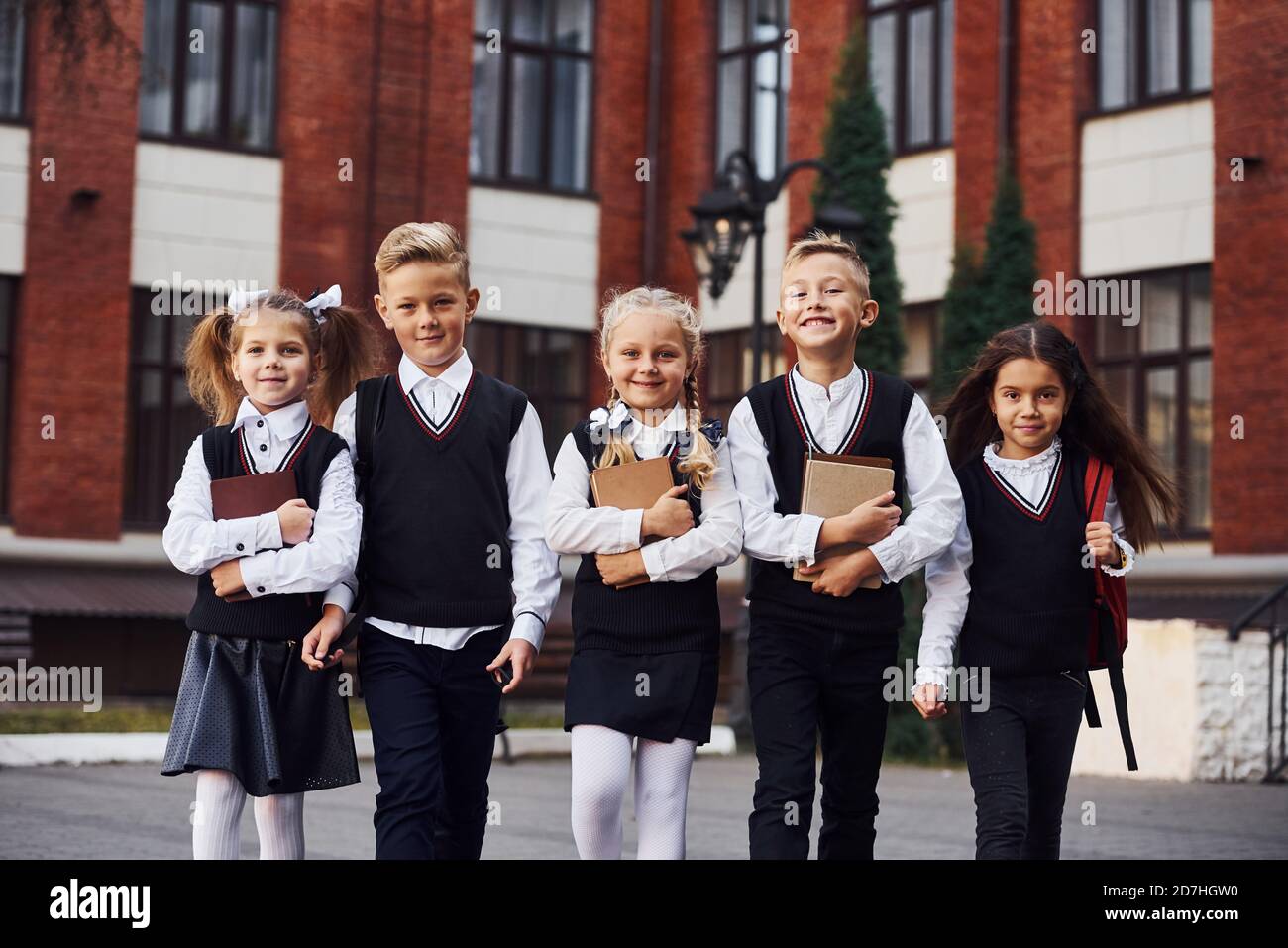 Gruppo di bambini in uniforme scolastica che è all'aperto insieme vicino all'edificio dell'istruzione Foto Stock