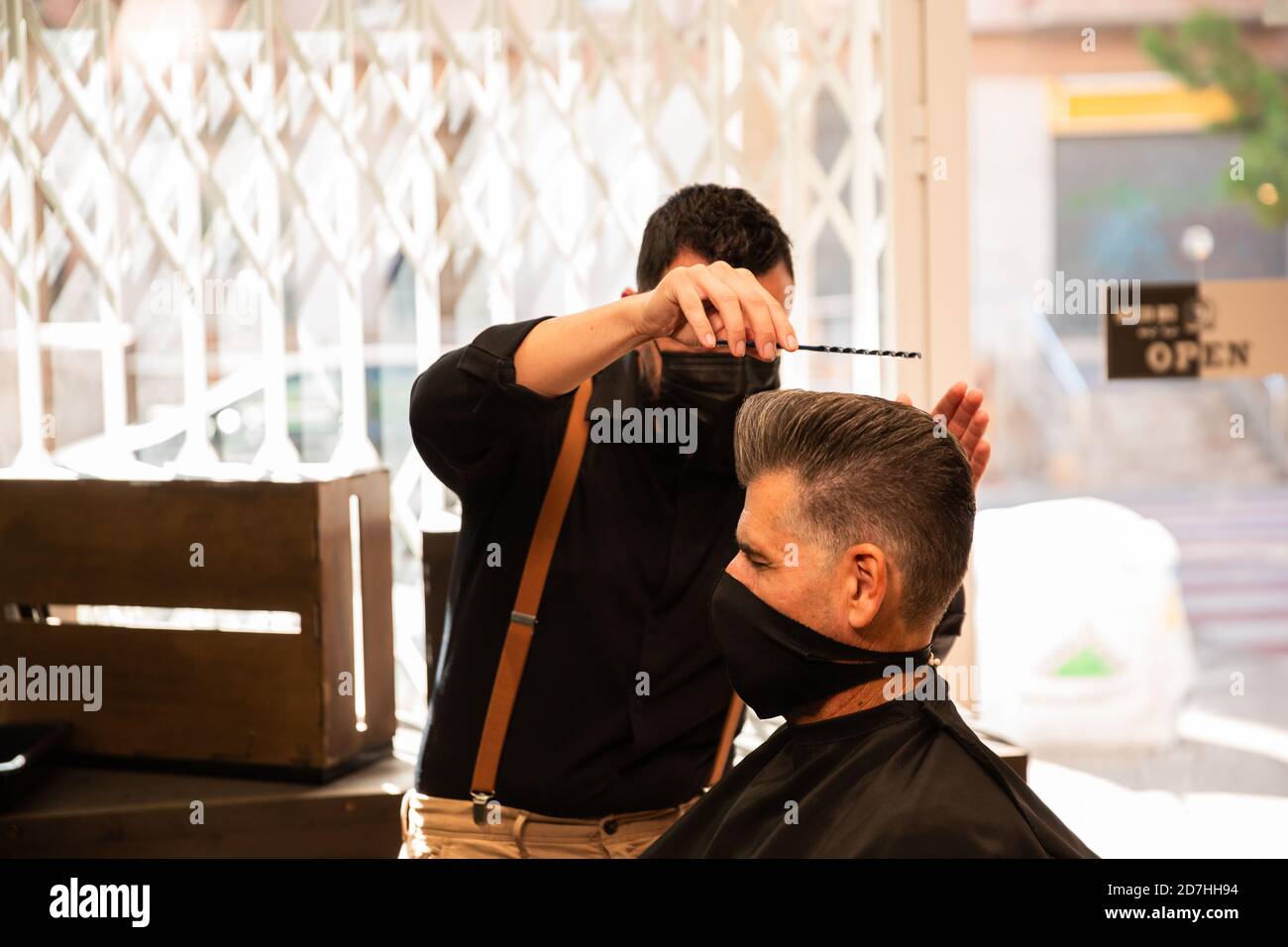 in un barbiere un barbiere combe un uomo cresciuto con la mano e il pettine, indossano maschere per la prevenzione del coronavirus pandemico. il cliente è seduto. anche Foto Stock