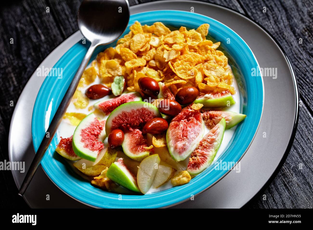 Sana colazione del mattino: Ciotola blu con yogurt naturale con fiocchi di mais croccanti, fichi, pera serviti su sfondo di legno nero, vista dall'alto, clos Foto Stock