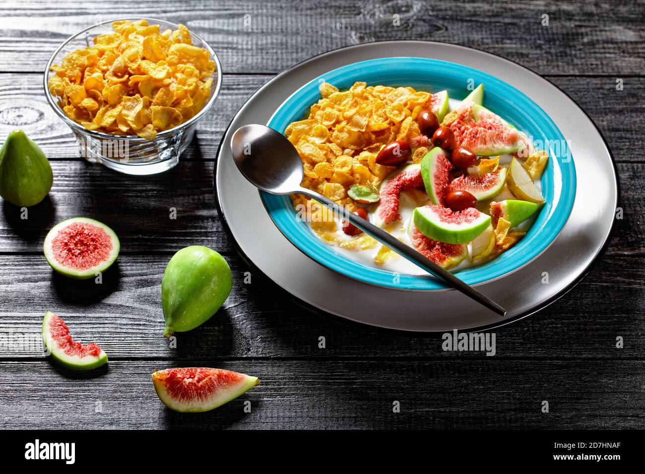 Sana colazione del mattino: Ciotola blu con yogurt naturale con fiocchi di mais croccanti, fichi, pera serviti su sfondo di legno nero, vista dall'alto, clos Foto Stock