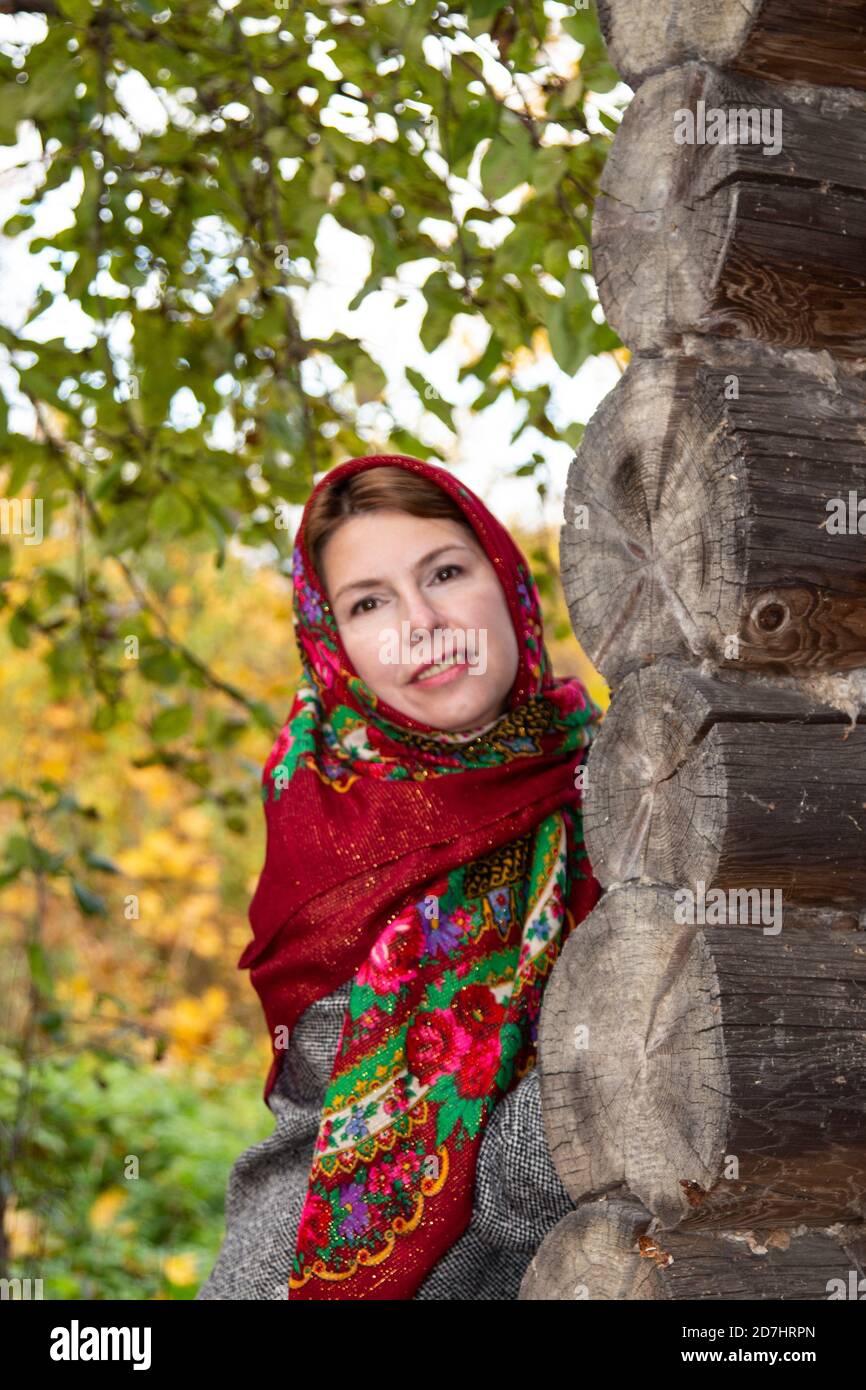 Una giovane donna in un tradizionale copricapo russo si affaccia dietro  l'angolo di una casa di legno. Fazzoletto Pavlovsk. Yaroslavl Russia  10.10.2019 Foto stock - Alamy