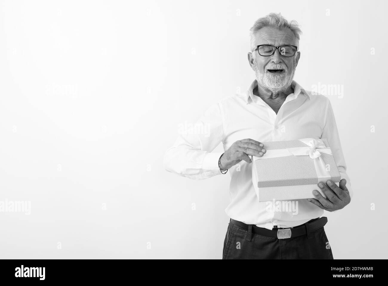 Studio shot di felice senior barbuto uomo sorridente durante l'apertura della confezione regalo gli occhi chiusi contro uno sfondo bianco Foto Stock