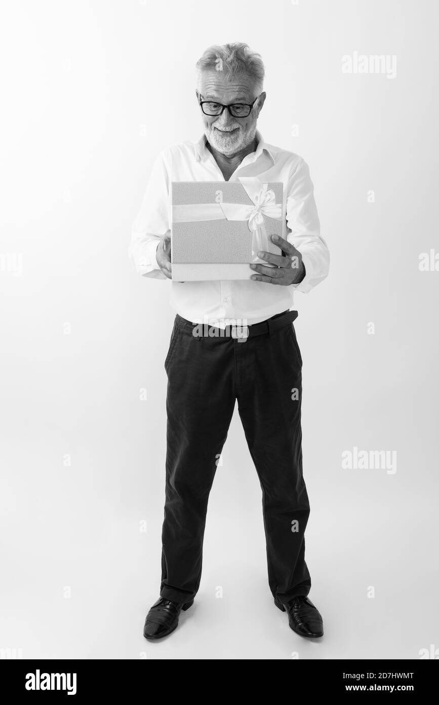 Corpo pieno colpo di felice senior barbuto uomo sorridente e in piedi durante le operazioni di apertura della confezione regalo contro uno sfondo bianco Foto Stock