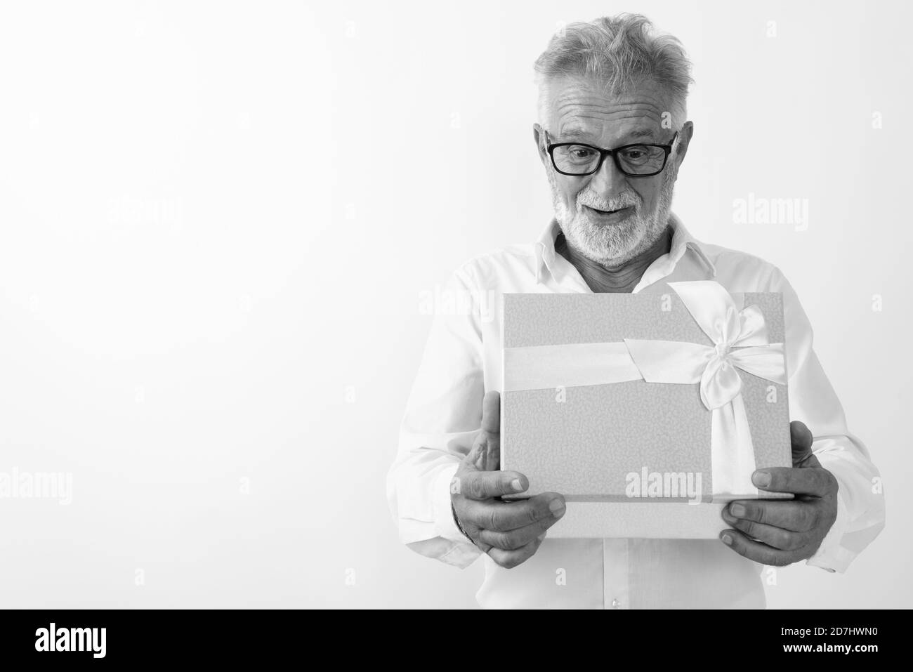 Studio shot di felice senior uomo barbuto sorridere mentre guardando scioccato durante l'apertura della confezione regalo con occhiali contro uno sfondo bianco Foto Stock