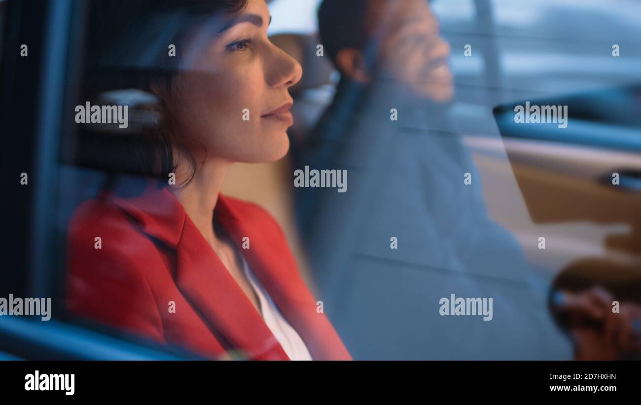 Bella donna e il suo maschio Partner Riding nella sede posteriore di un'auto. È sera nella Big City. Camera Shot dall'esterno del veicolo. Foto Stock