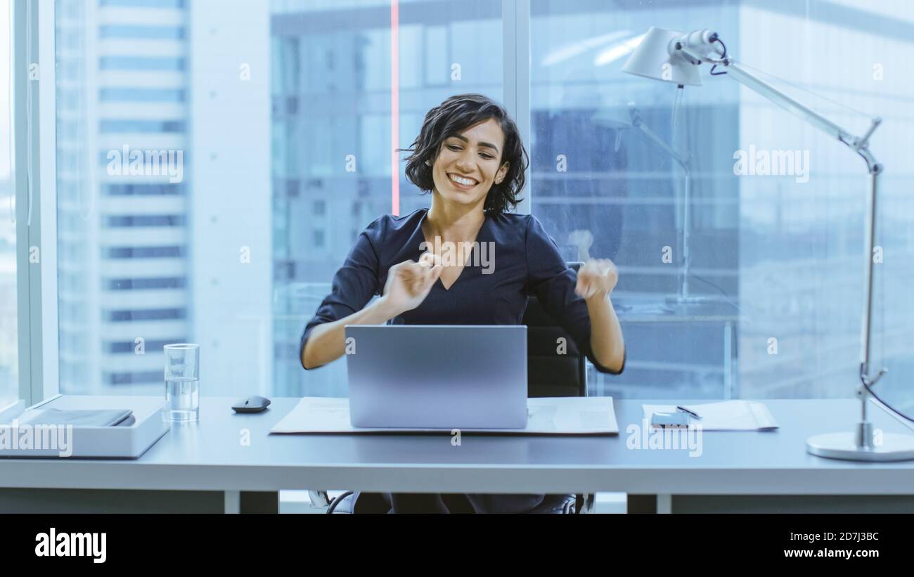 Ritratto della bella Businesswoman Dancing mentre si siede alla sua scrivania. Donna felice e di successo che celebra le vendite record. Foto Stock
