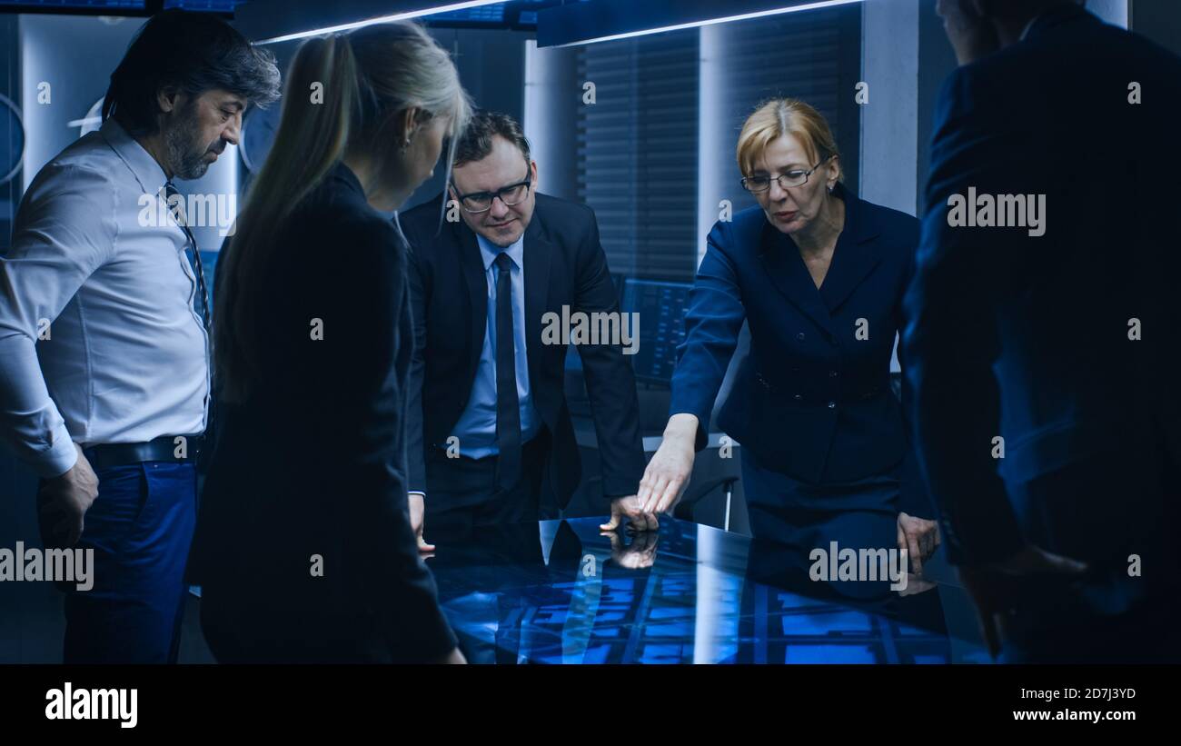 Team diversificato di Agenti di intelligence governativi in piedi intorno al tavolo digitale touch screen e il monitoraggio sospetto, Senior Officer fa Interactive Foto Stock