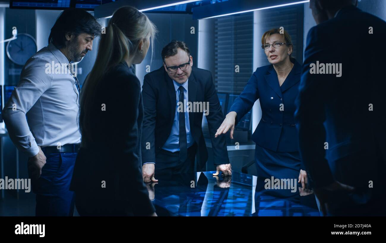 Team diversificato di Agenti di intelligence governativi in piedi intorno al tavolo digitale touch screen e il monitoraggio sospetto, Senior Officer fa Interactive Foto Stock