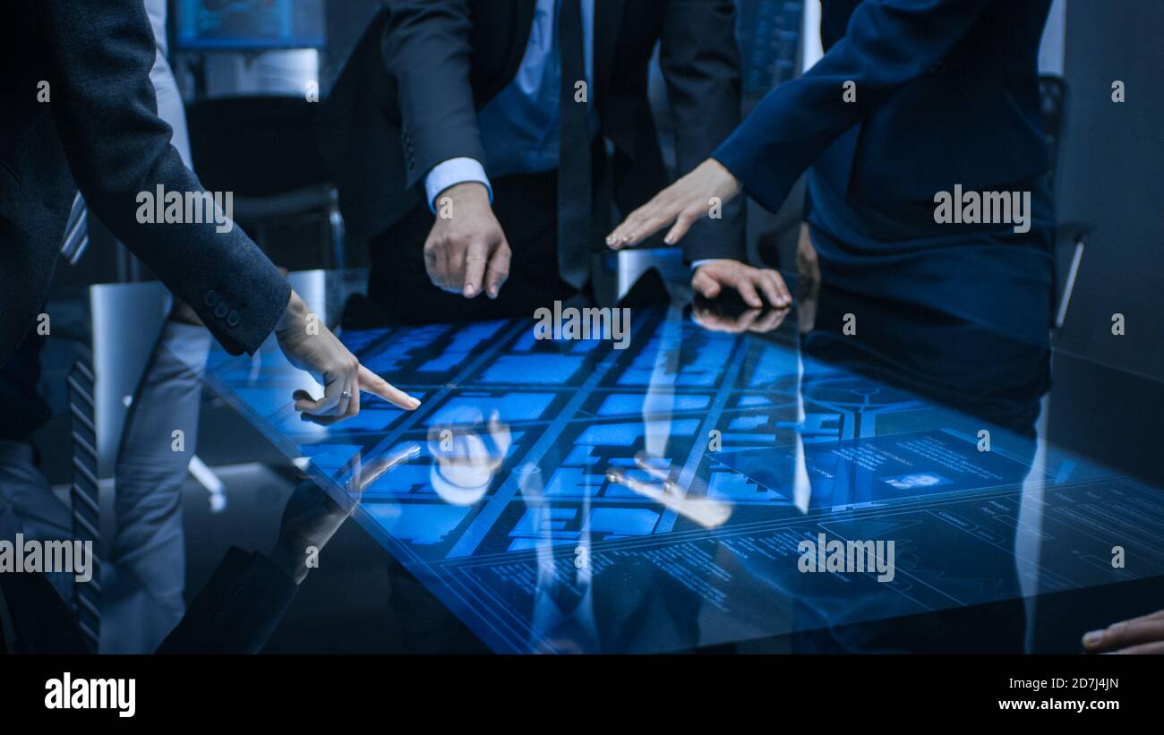 Diversi team di agenti di intelligence governativi che si aggirano attorno al tavolo digitale con schermo a sfioramento e al satellite Tracking sospettano, puntando al display. Grande Foto Stock