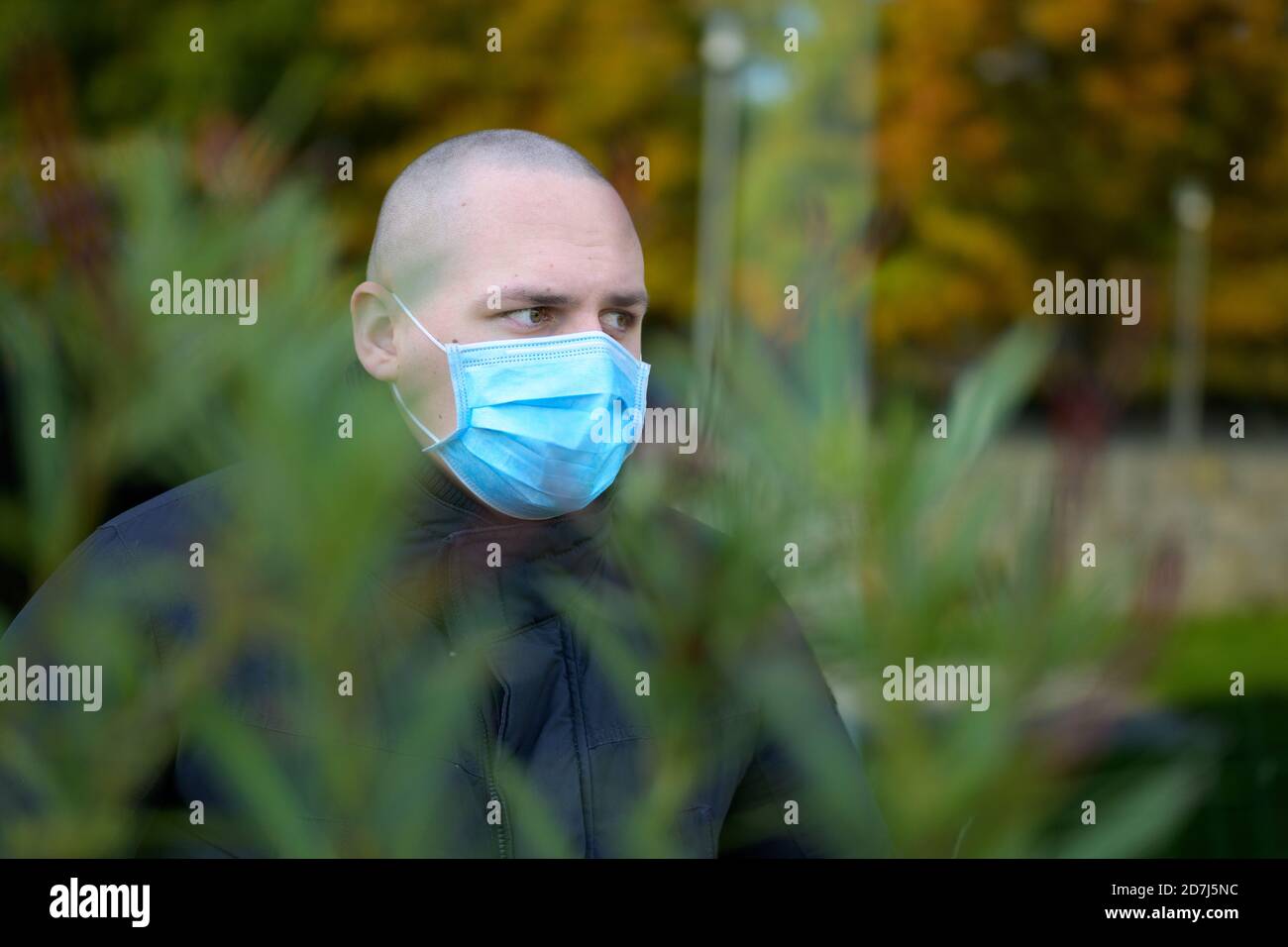 Nuovo stile di vita normale indossando una maschera per il viso all'aperto con un vista attraverso il verde di un giovane uomo nei suoi venti anni indossare una maschera chirurgica monouso Foto Stock