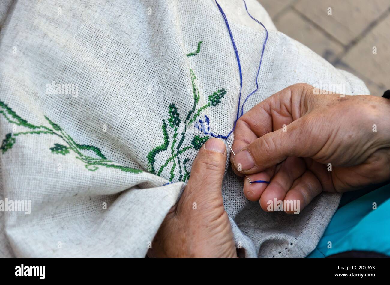 Mani di una donna anziana che ricamo un motivo floreale a punto croce su tessuto di lino. Ricamo, lavorazione a mano, concetto di agugliata. Primo piano Foto Stock