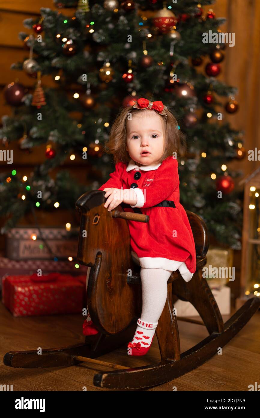 bambina in un vestito rosso festivo su un cavallo oscillante di legno. Le  feste di Natale sono un periodo favoloso per i bambini Foto stock - Alamy