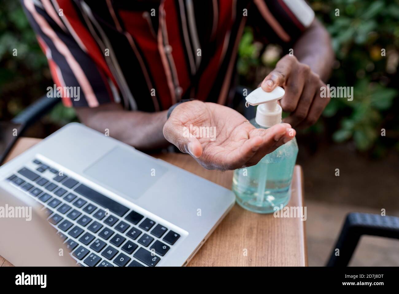 Giovane uomo che usa l'igienizzatore per le mani mentre si è seduti con il computer portatile caffè Foto Stock