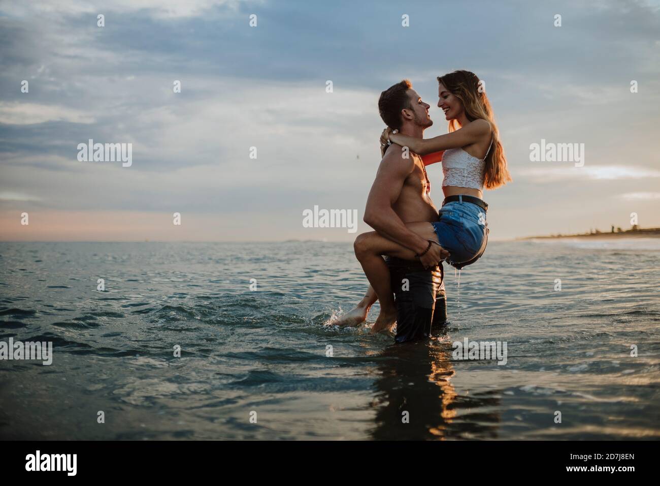 Uomo che porta donna mentre si è in piedi in acqua durante il tramonto a. spiaggia Foto Stock