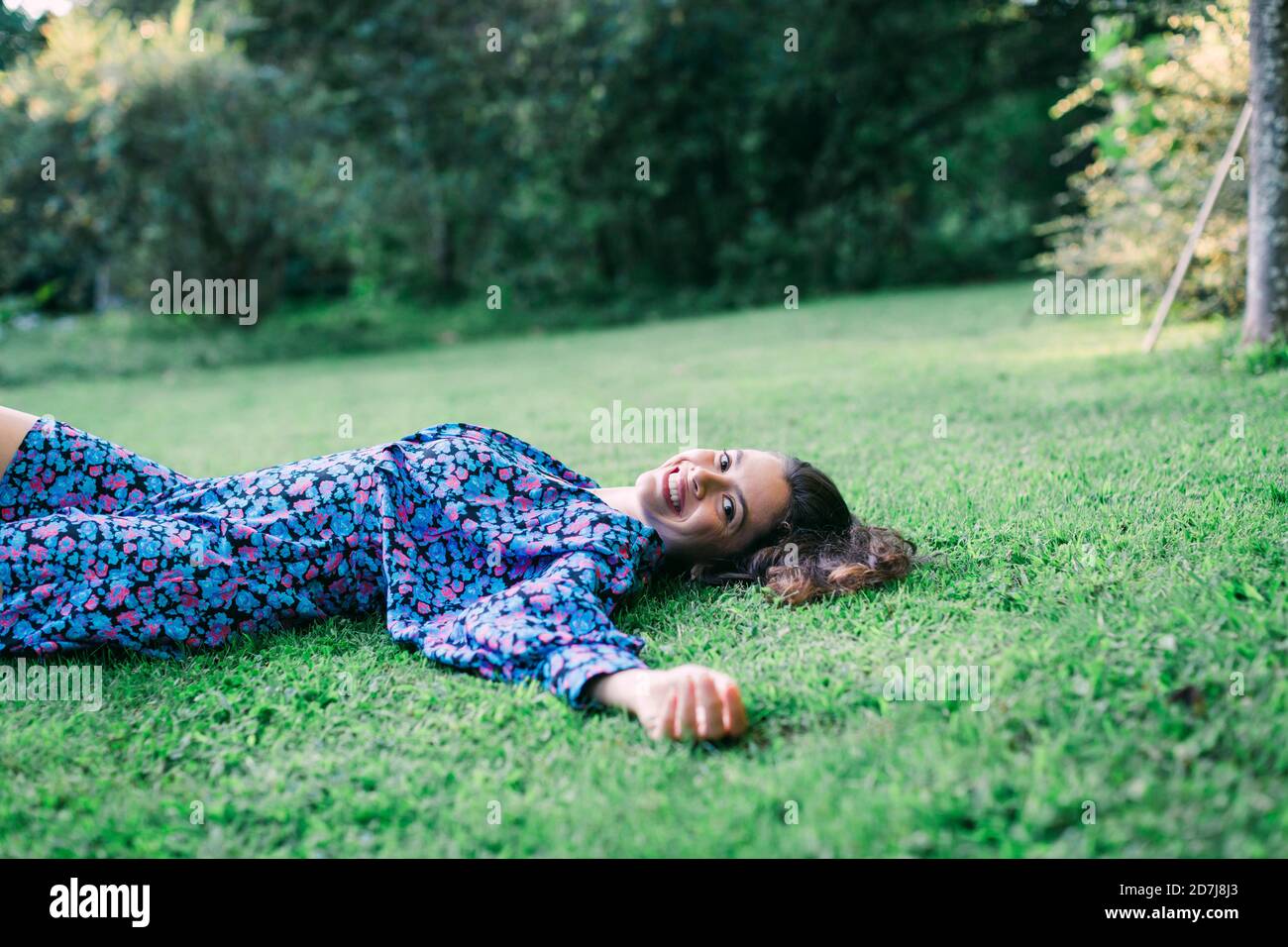 Giovane donna allegra che riposa su terra erbosa nel parco Foto Stock