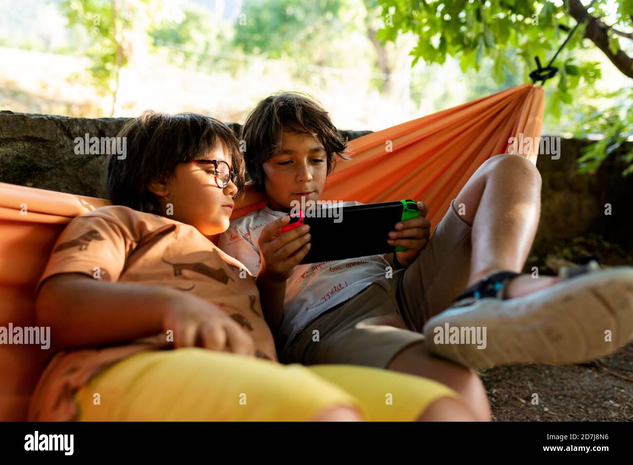 Fratelli giocando video giochi mentre si sdraia su amaca in cortile Foto Stock