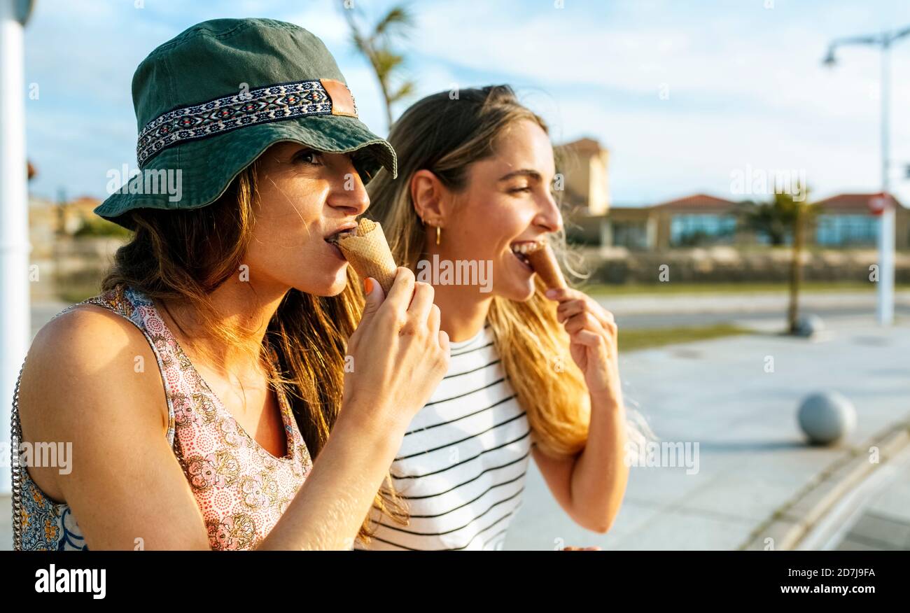 Giovani donne che guardano via mentre mangiano il gelato in città durante il fine settimana Foto Stock