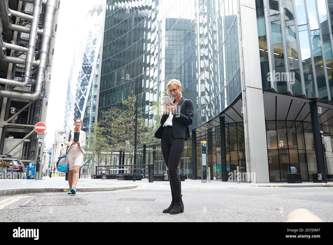 Donne d'affari che usano smartphone contro gli edifici degli uffici in centro Foto Stock