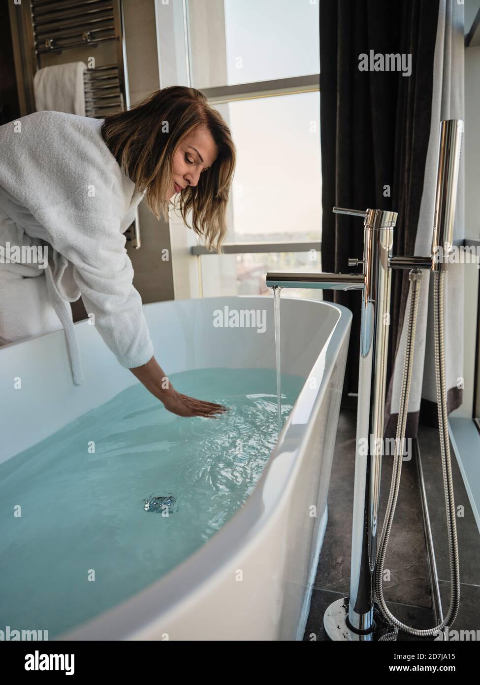 Donna anziana che si piega sopra mentre esamina la temperatura nella vasca da bagno a. hotel di lusso Foto Stock