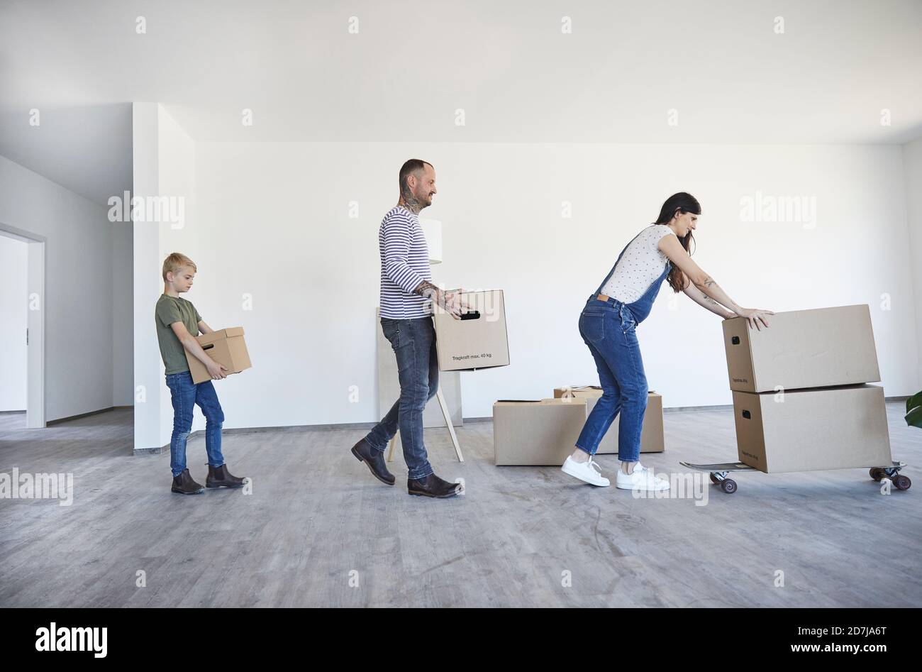 Famiglia che tiene scatole di cartone sullo skateboard in casa nuova Foto Stock