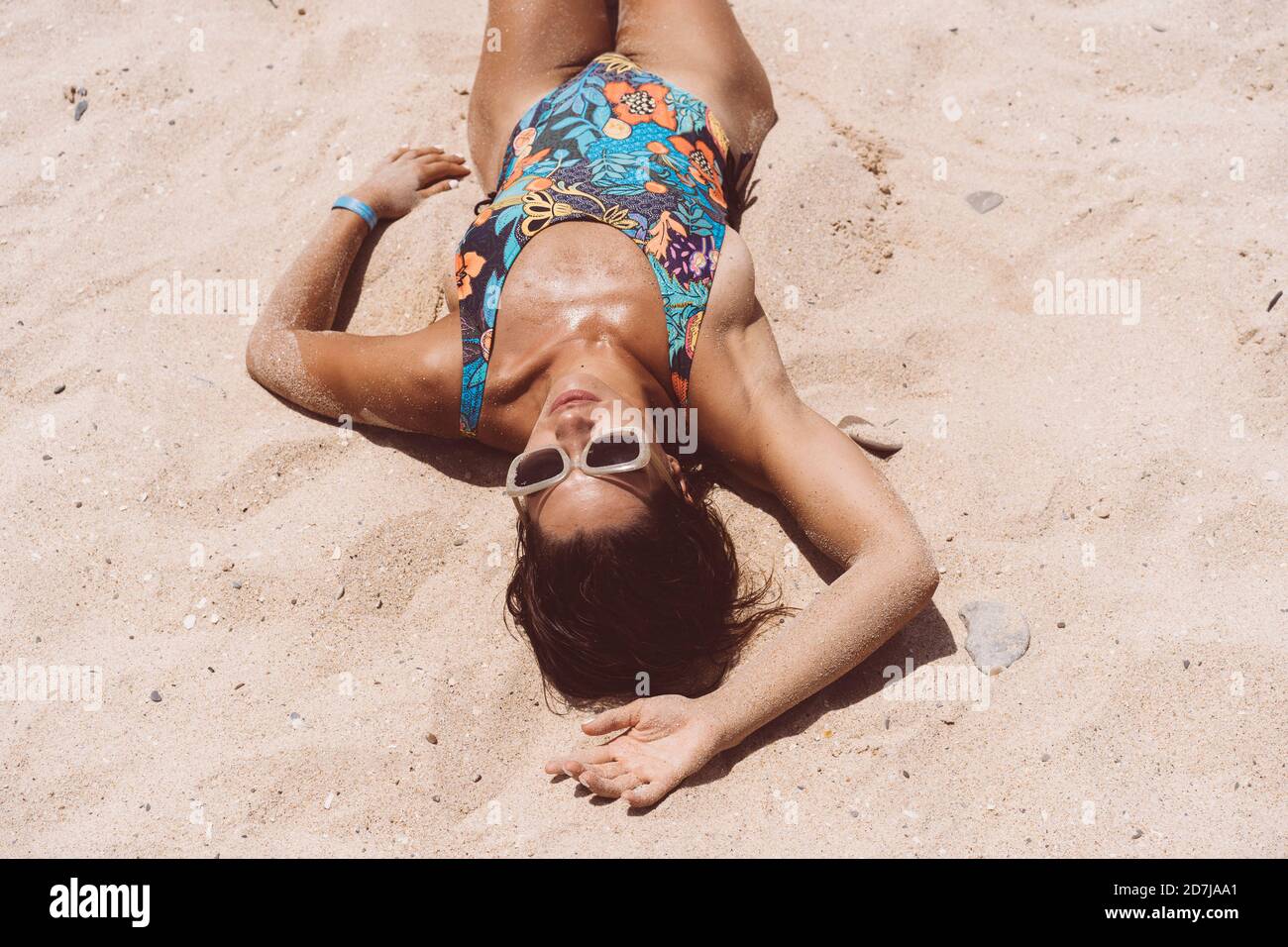 Donna mid adulta che indossa il bodysuit sdraiato sulla spiaggia di Valdevaqueros in giornata di sole, Tarifa, Spagna Foto Stock