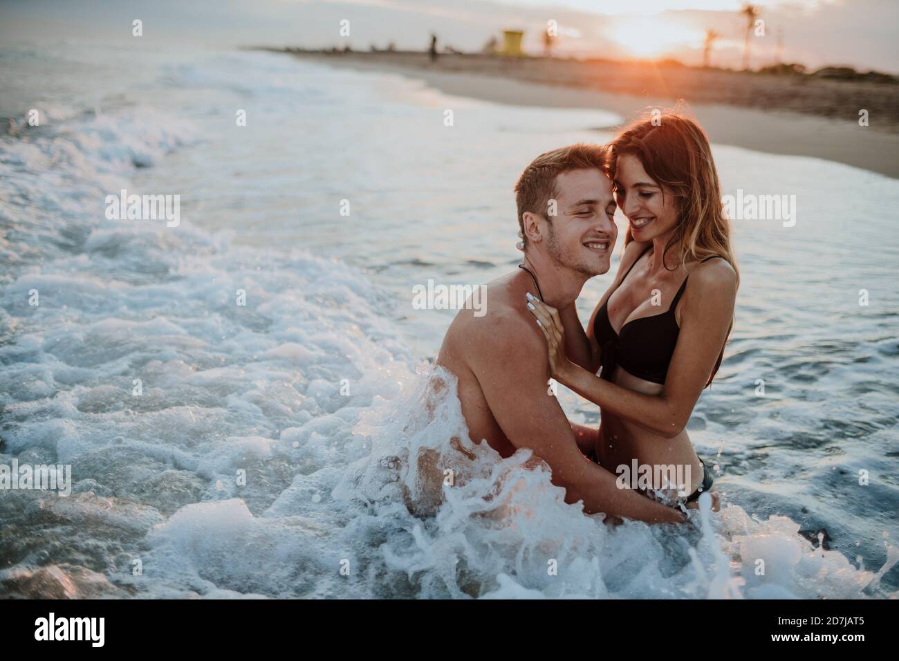 Una coppia sorridente si diverta mentre si siede in acqua sulla spiaggia Foto Stock