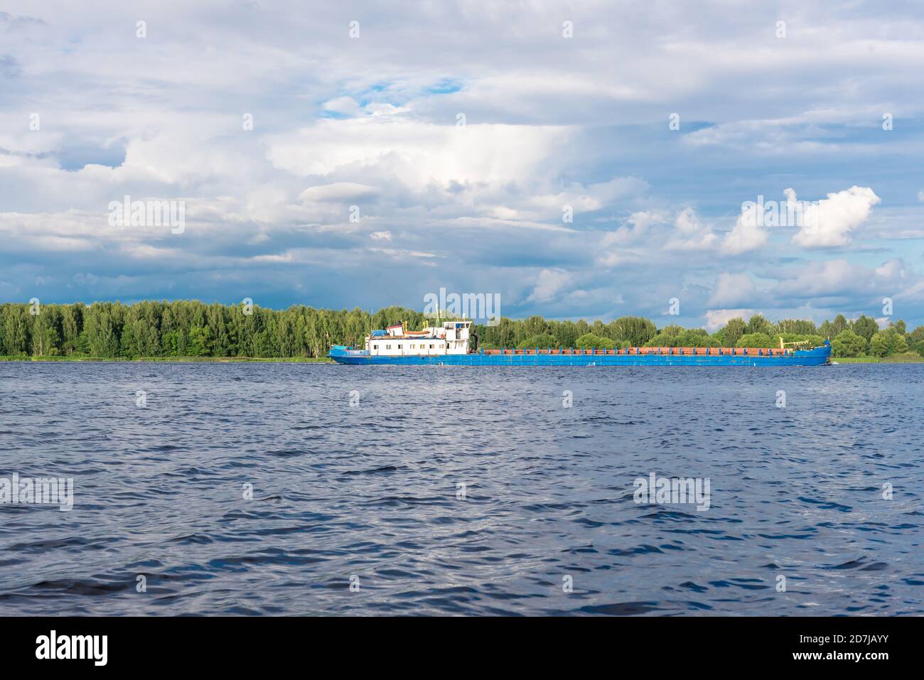 La nave da carico veleggia lungo il tranquillo fiume sotto il cielo con le nuvole Foto Stock