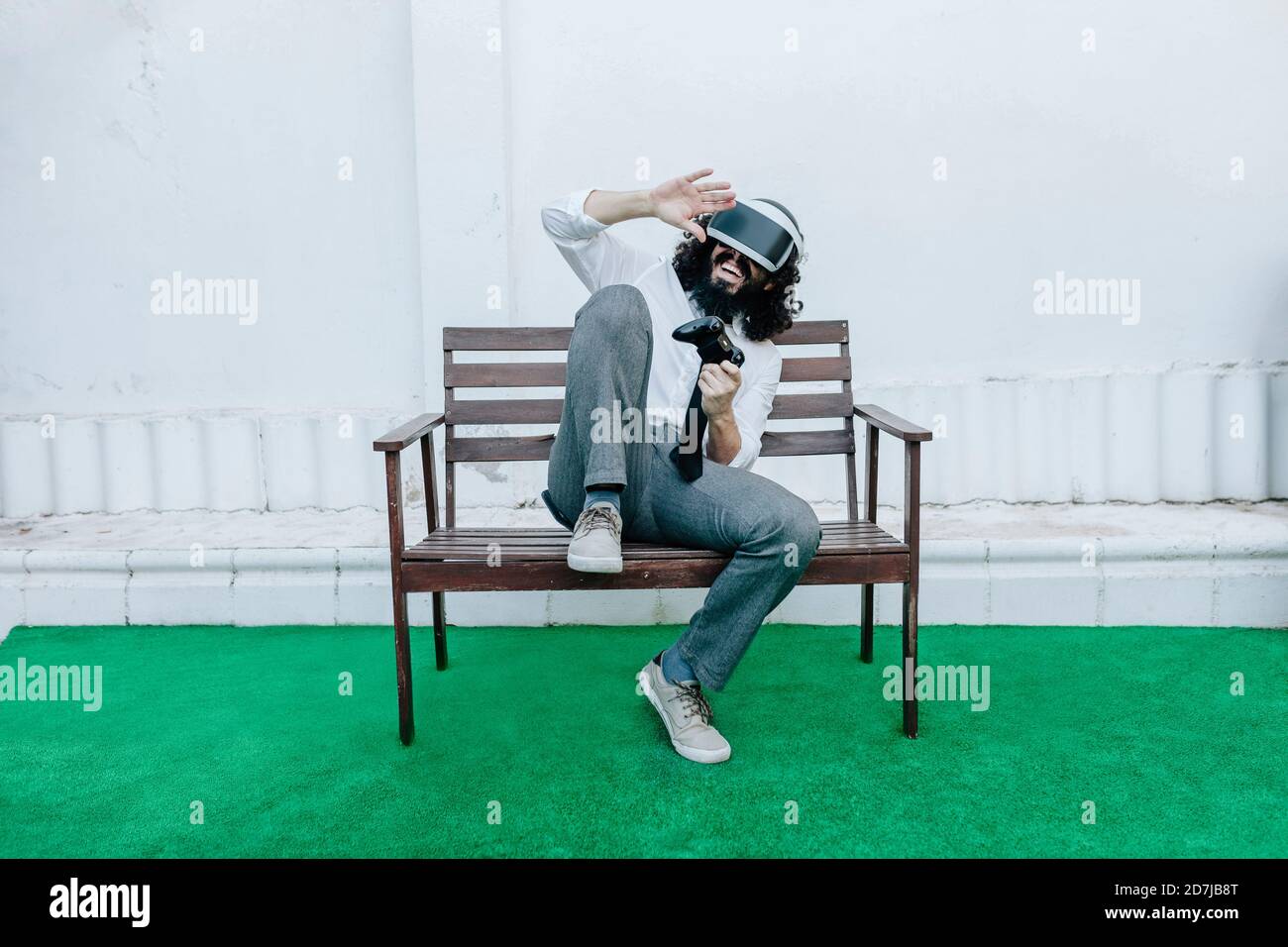 Uomo che gioca a un videogioco utilizzando occhiali in realtà virtuale mentre si è seduti in cortile Foto Stock