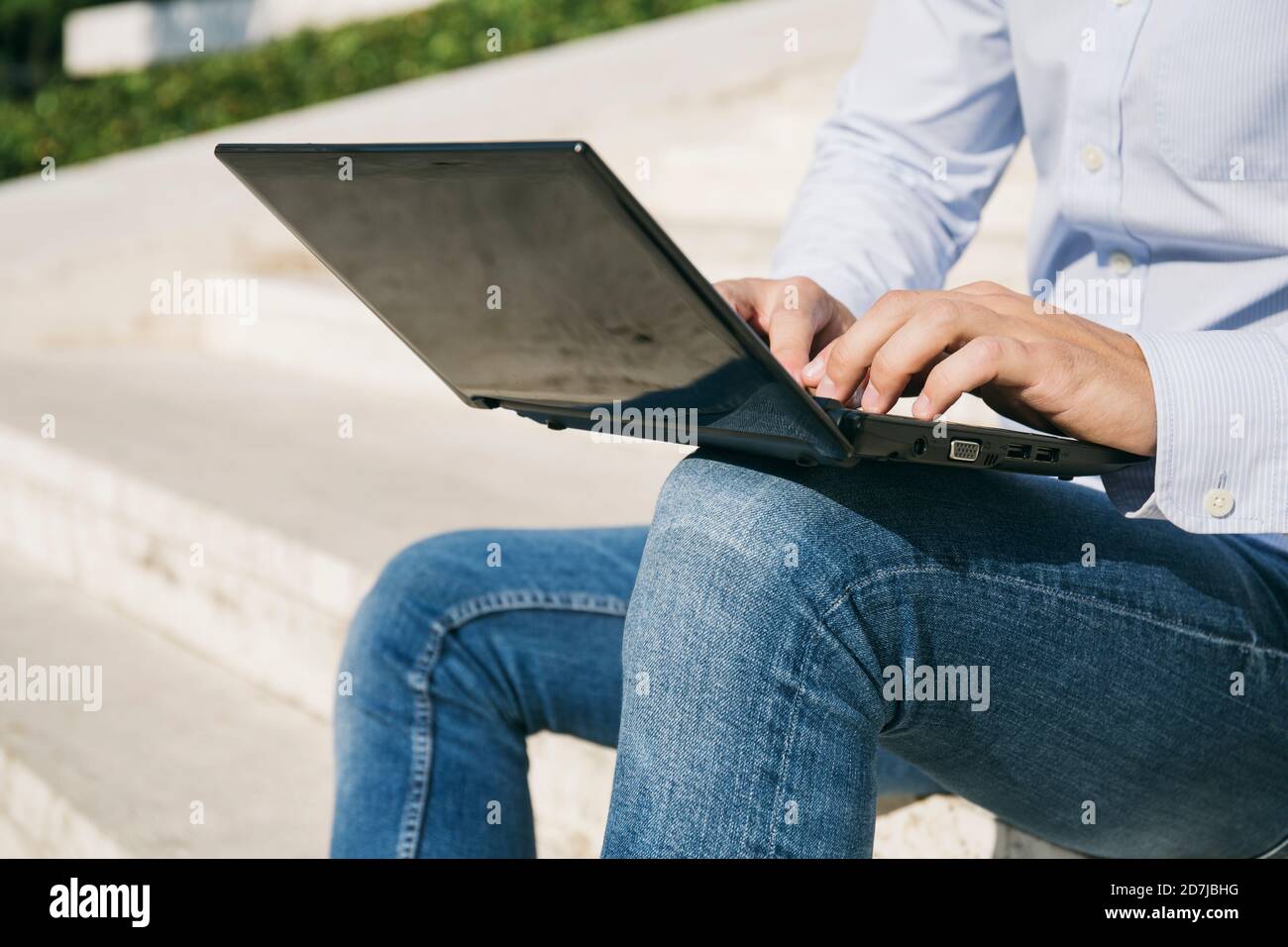 Uomo che scrive sul computer portatile mentre si siede all'aperto durante la giornata di sole Foto Stock
