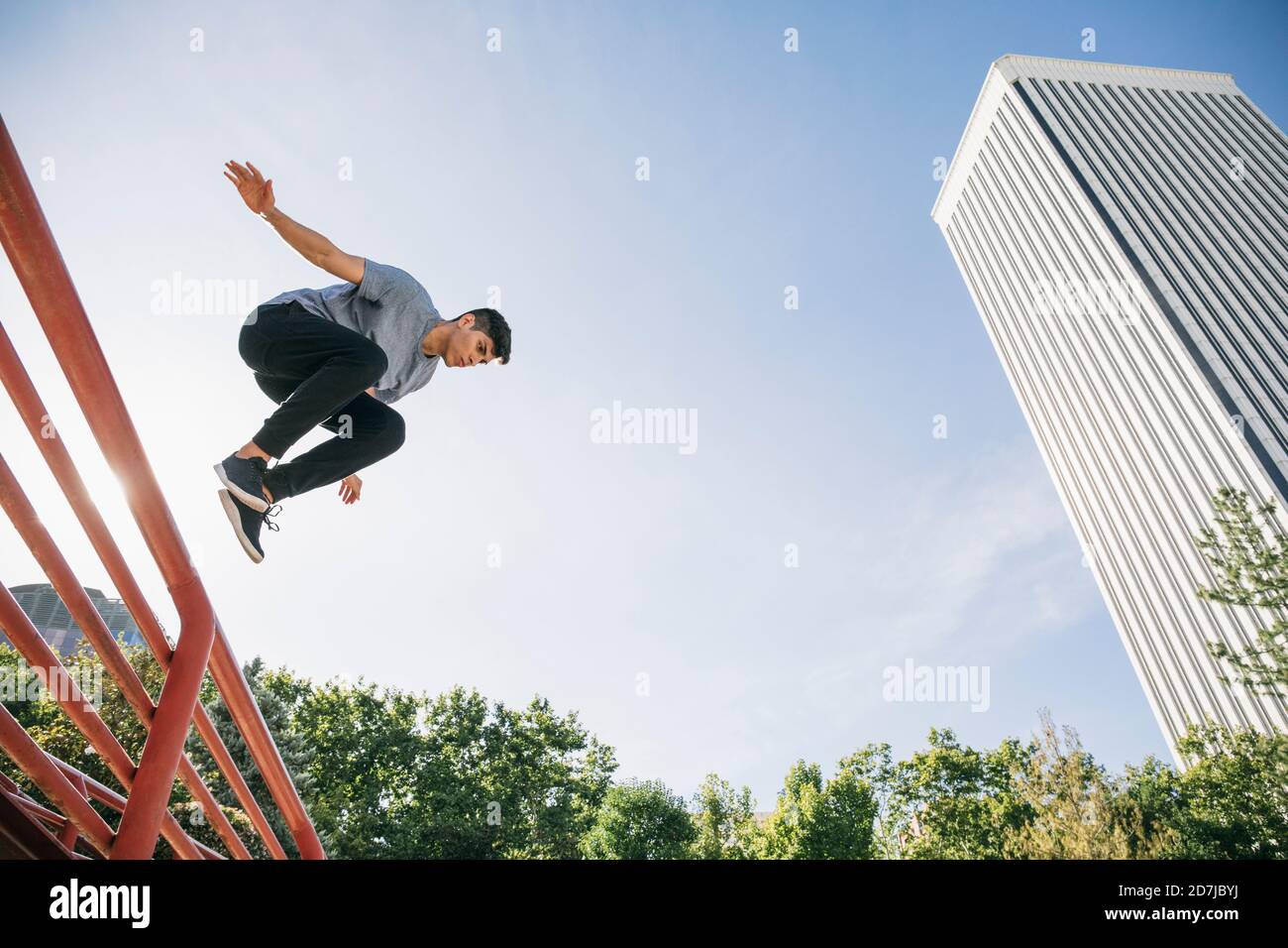 Giovane uomo che esegue parkour sopra ringhiera contro cielo chiaro dentro città Foto Stock