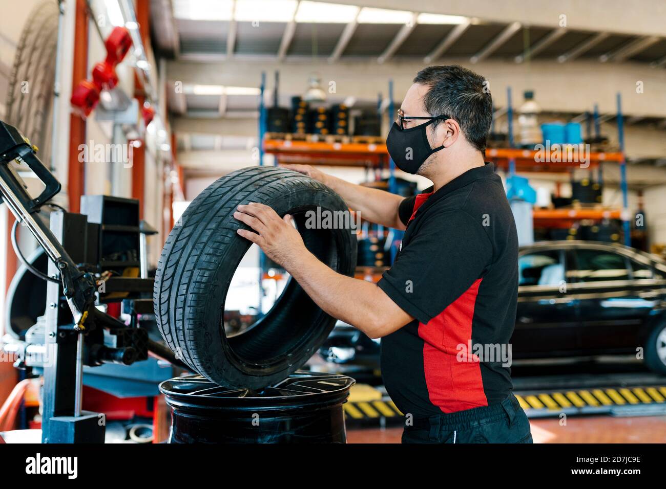 Meccanico che indossa maschera esame pneumatico in officina di riparazione auto Foto Stock