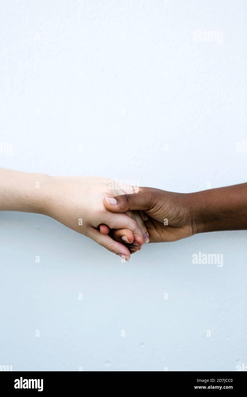 Gli amici scuotono la mano contro la parete bianca Foto Stock