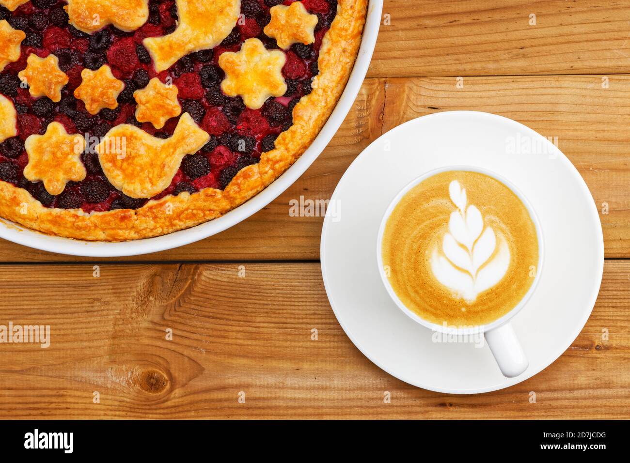 Primo piano torta di frutti di bosco con frusta fatta in casa e una tazza bianca di cappuccino di caffè su un tavolo di legno. Foto Stock