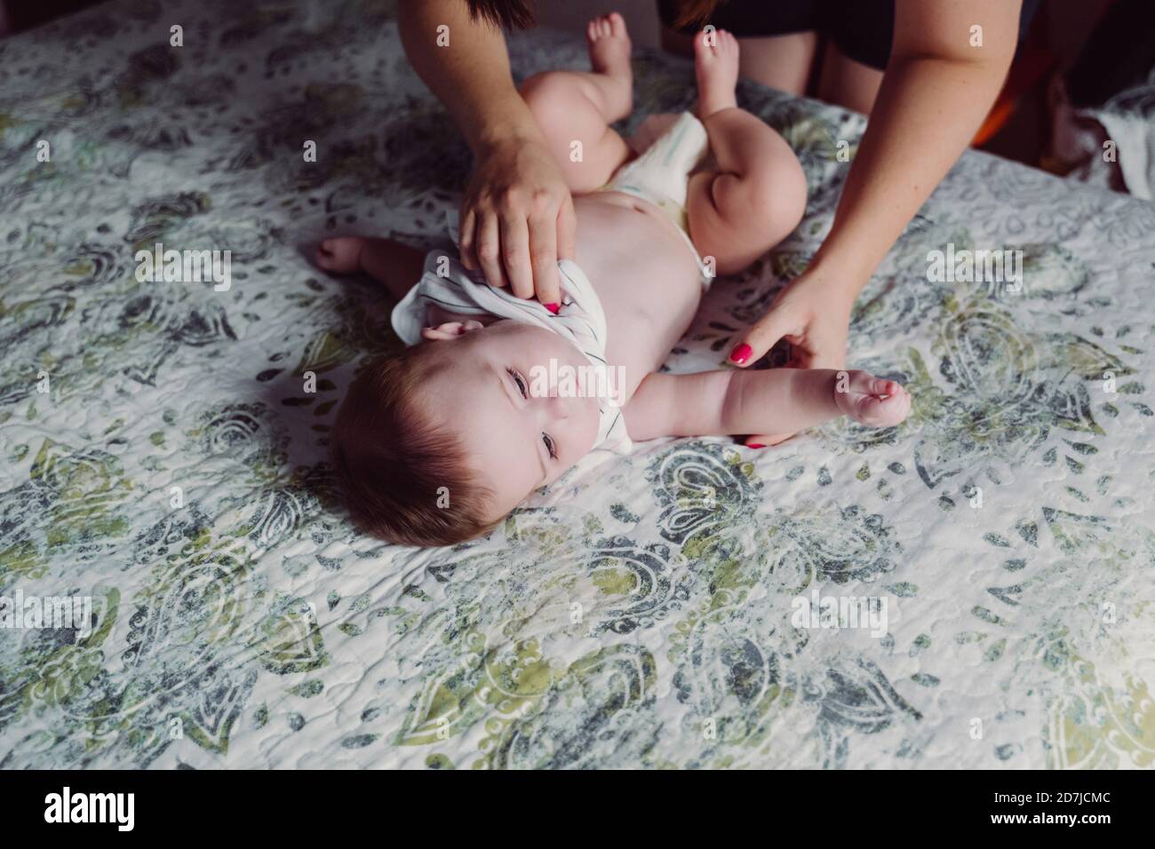 Mani di madre che vestiscono la figlia del bambino che si trova sul letto a casa Foto Stock