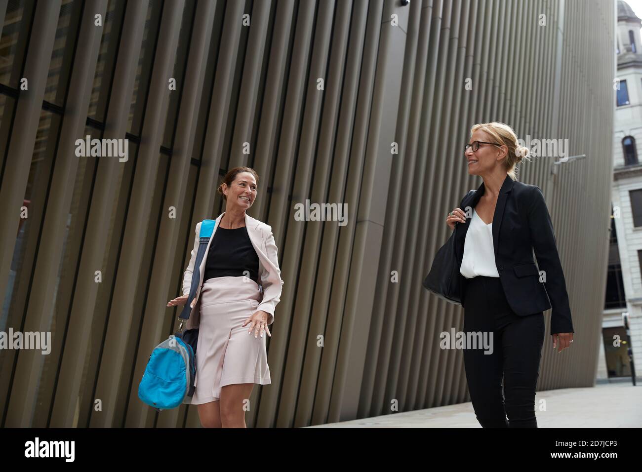 Sorridi le donne che parlano mentre camminano per la costruzione dell'ufficio dentro in centro Foto Stock