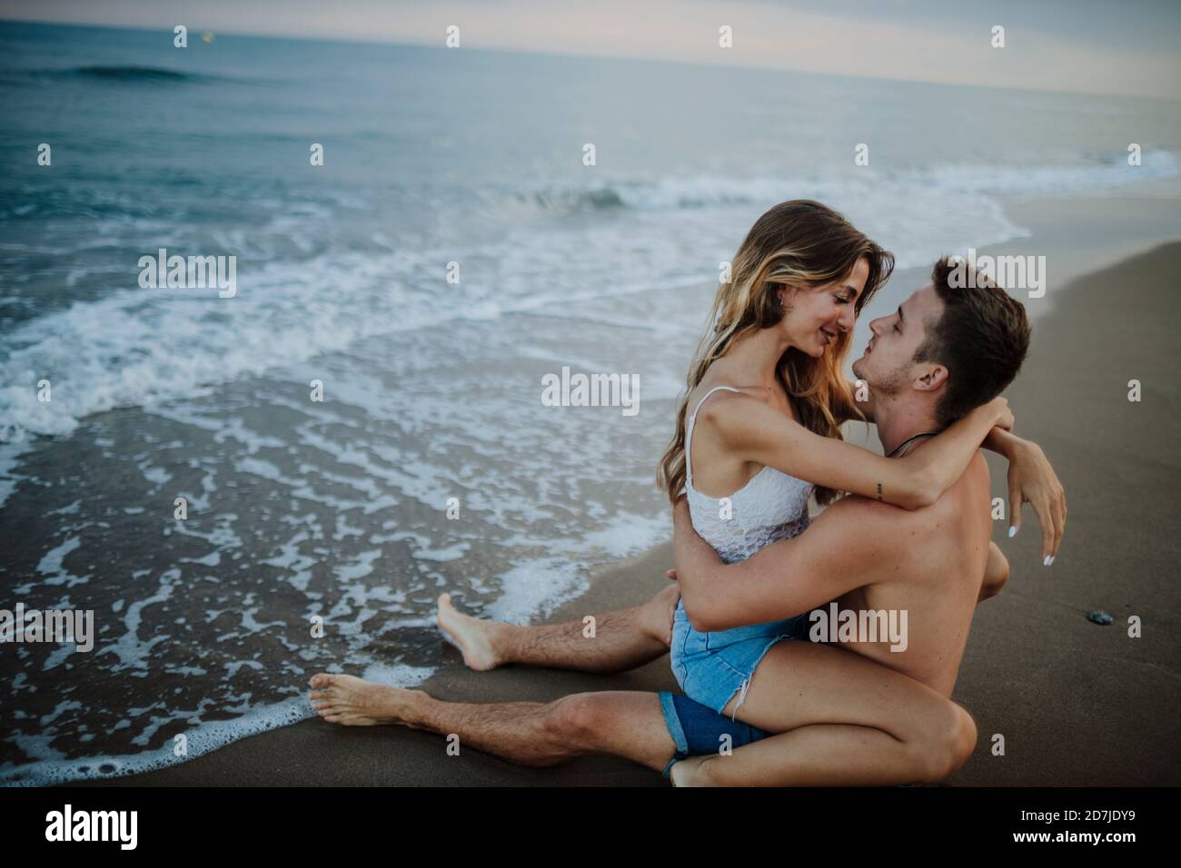 Giovane coppia che fa romanticismo mentre si siede sulla spiaggia Foto Stock