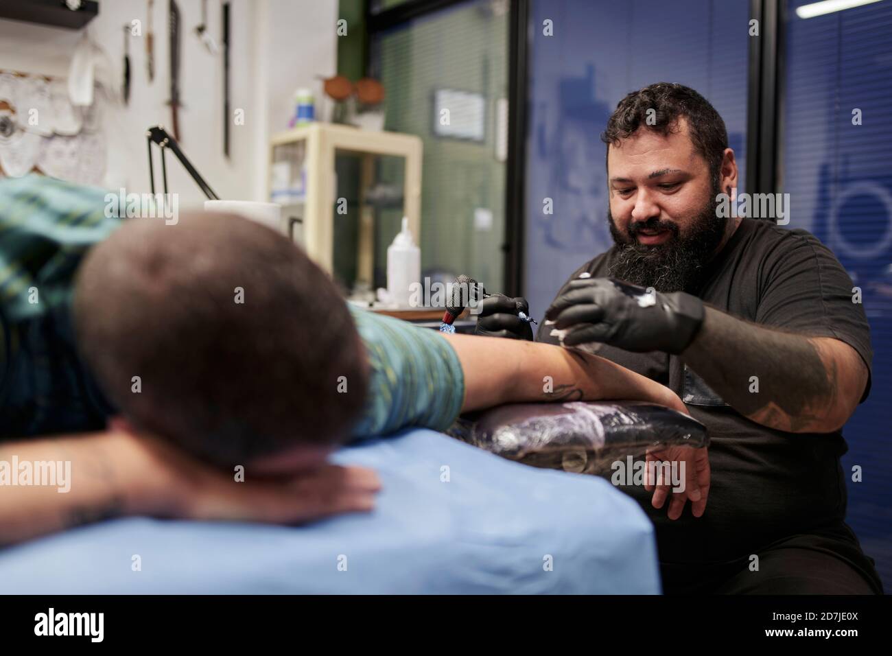 Artista bearded tatuando sulla mano dell'uomo dell'adulto medio che si stese sopra letto in studio Foto Stock