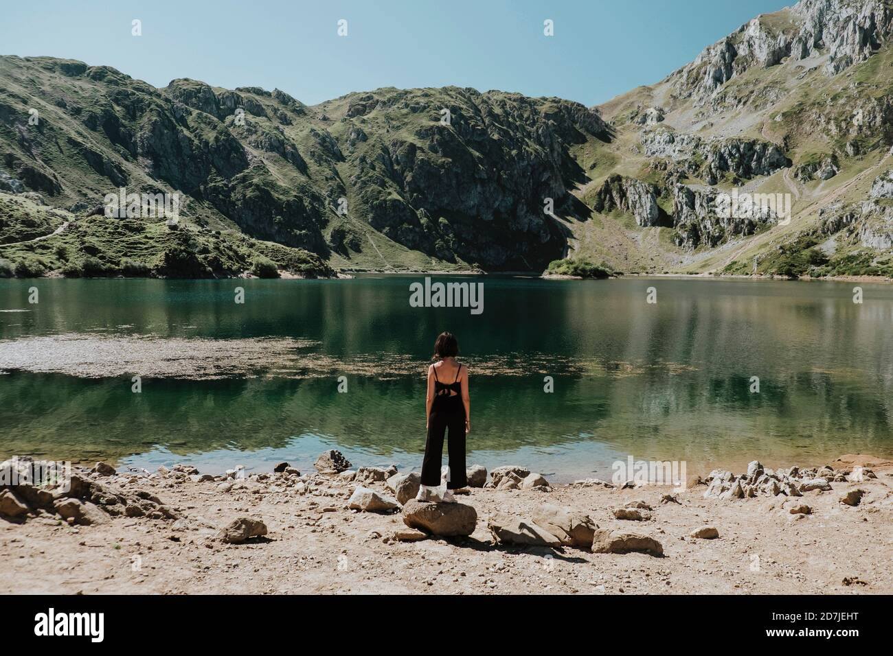 Donna che guarda il lago mentre si sta in piedi sulla pietra durante il giorno di sole Foto Stock