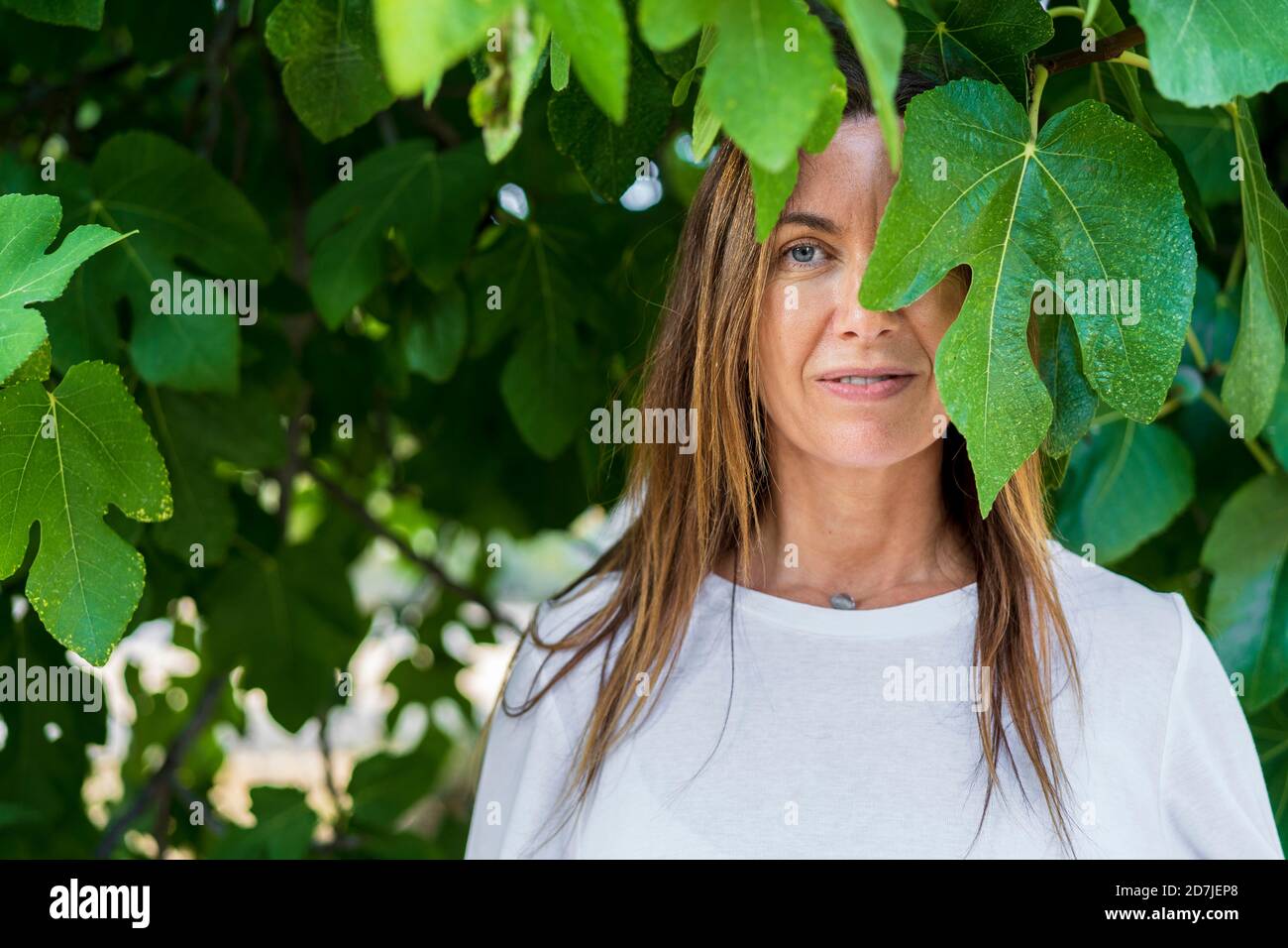 Donna matura con occhi blu in piedi sotto foglie verdi a. cortile posteriore Foto Stock