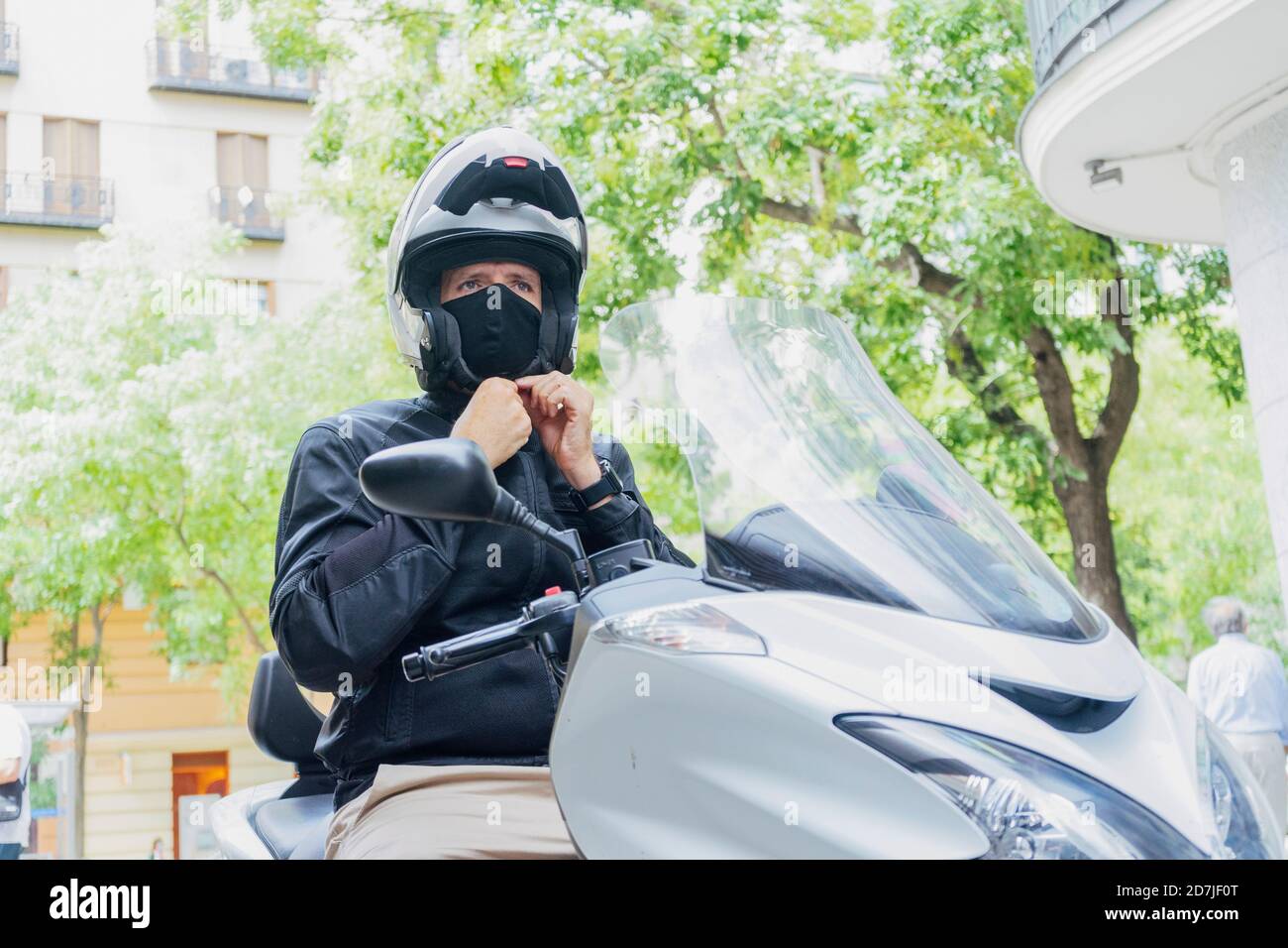Biker maschile che indossa il casco mentre si siede su scooter Foto Stock