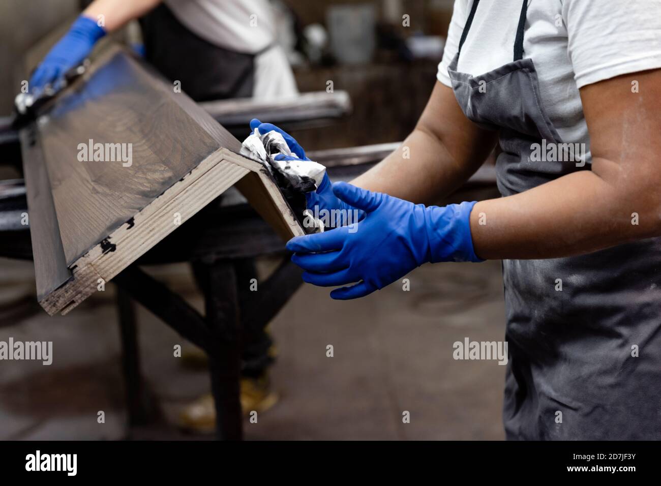 Carpentiere verniciatura legno con coworker che lavora in background in fabbrica Foto Stock