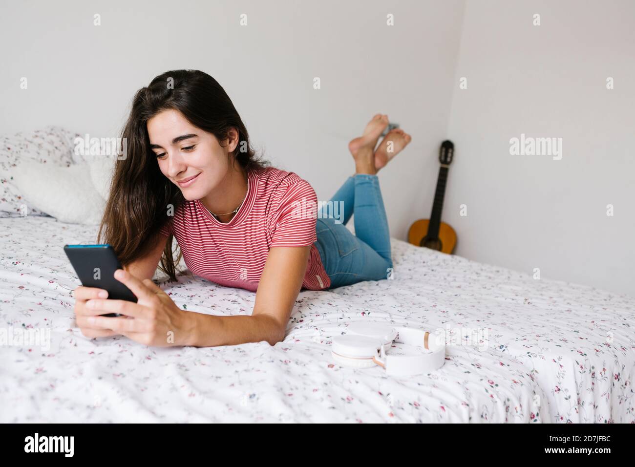 Donna sdraiata durante la messaggistica di testo su smartphone a. casa Foto Stock