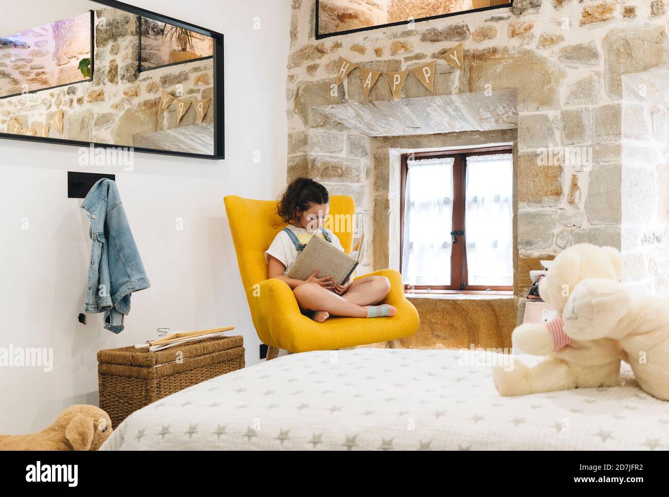 Ragazza che legge libro mentre sedendo sulla poltrona in camera da letto a. casa Foto Stock